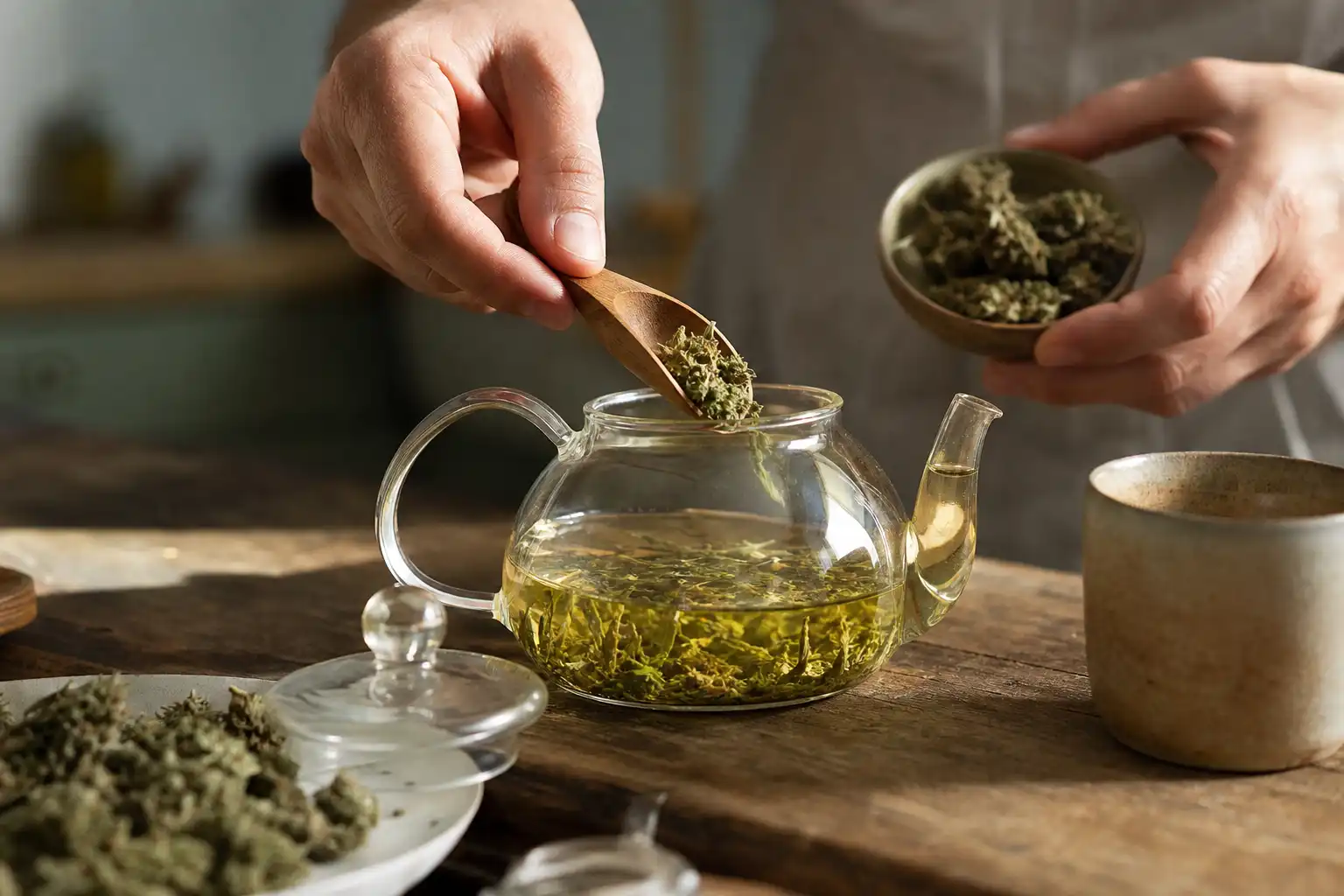 Des mains manipulent un objet, autour d'une infusion de chanvre et ses fleurs séchées, dans une cuisine.